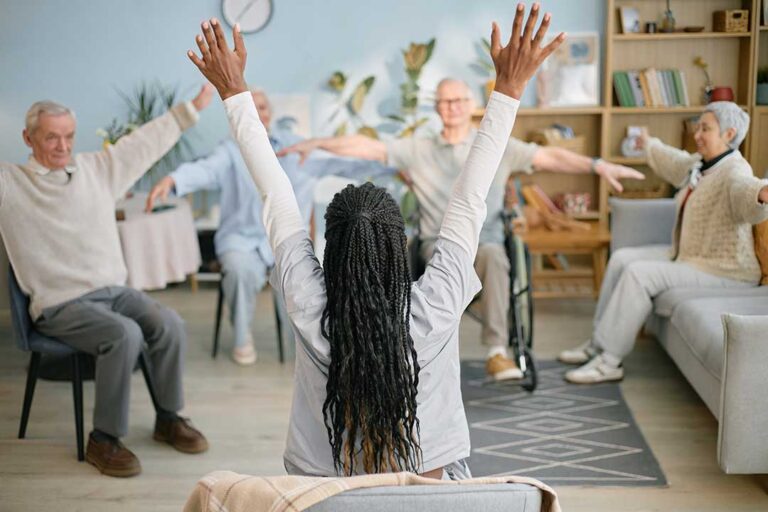 Older adults participate in a gentle group exercise session in a bright assisted living activity room.